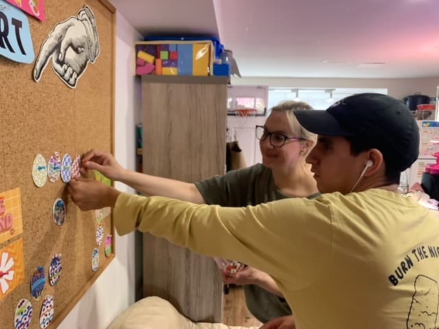 A Catching Stars participant and support person placing artwork on a board together.